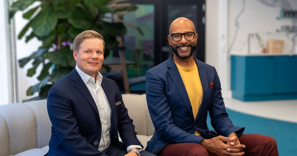 Jukka Holm ja Eric Coker istuvat toimiston sohvalla. Jukalla on tumma puvun takki ja Ericillä on tummansininen puvun takki.